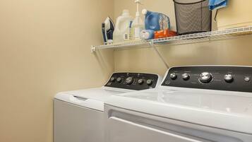 Un lave-linge à chargement frontal doté d’un panneau de commande, d’une étagère au-dessus pour ranger les produits de lessive et d’un panier à linge contenant une serviette.