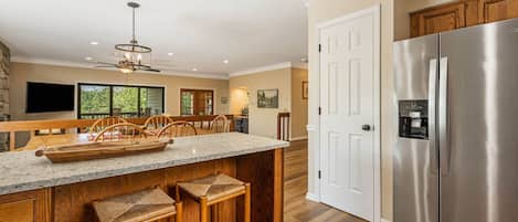 A modern kitchen with a large island, wooden bar stools, a stainless steel refrigerator, and a ceiling fan.