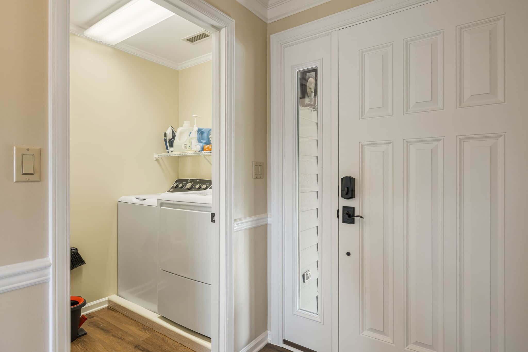 A laundry room with a washer and dryer, a shelf with cleaning supplies, and a white door with a keyhole.