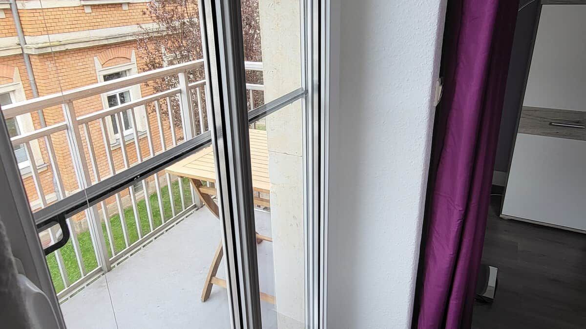Ein Zimmer mit Fenster und Blick auf einen Balkon mit Holztisch und Stühlen.