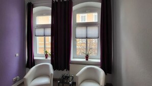 A room with two windows, purple curtains, a radiator, a small table with a glass top, and two white chairs. - Beautiful Vacation Rental in Dresden (Dresden)