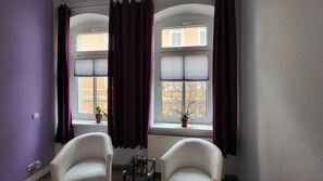 A room with two windows, purple curtains, a radiator, a small table with a glass top, and two white chairs. - Beautiful Vacation Rental in Dresden (Dresden)