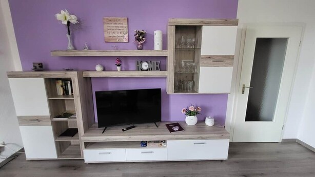 A living room with a flat-screen TV, wooden shelves, and a door. - Beautiful Vacation Rental in Dresden (Dresden)