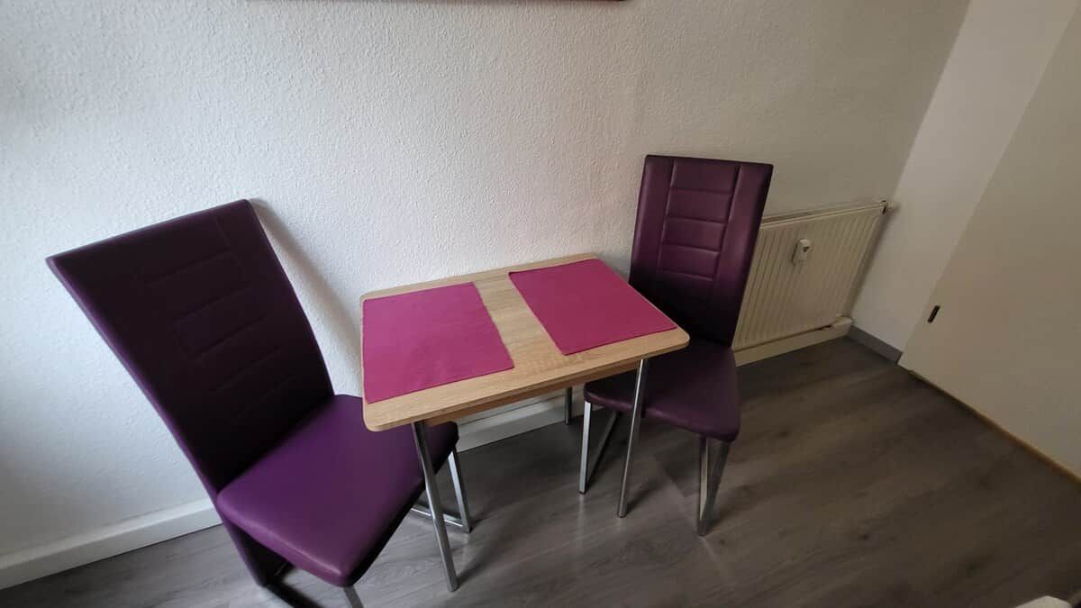 A small room with a wooden table and two purple chairs.