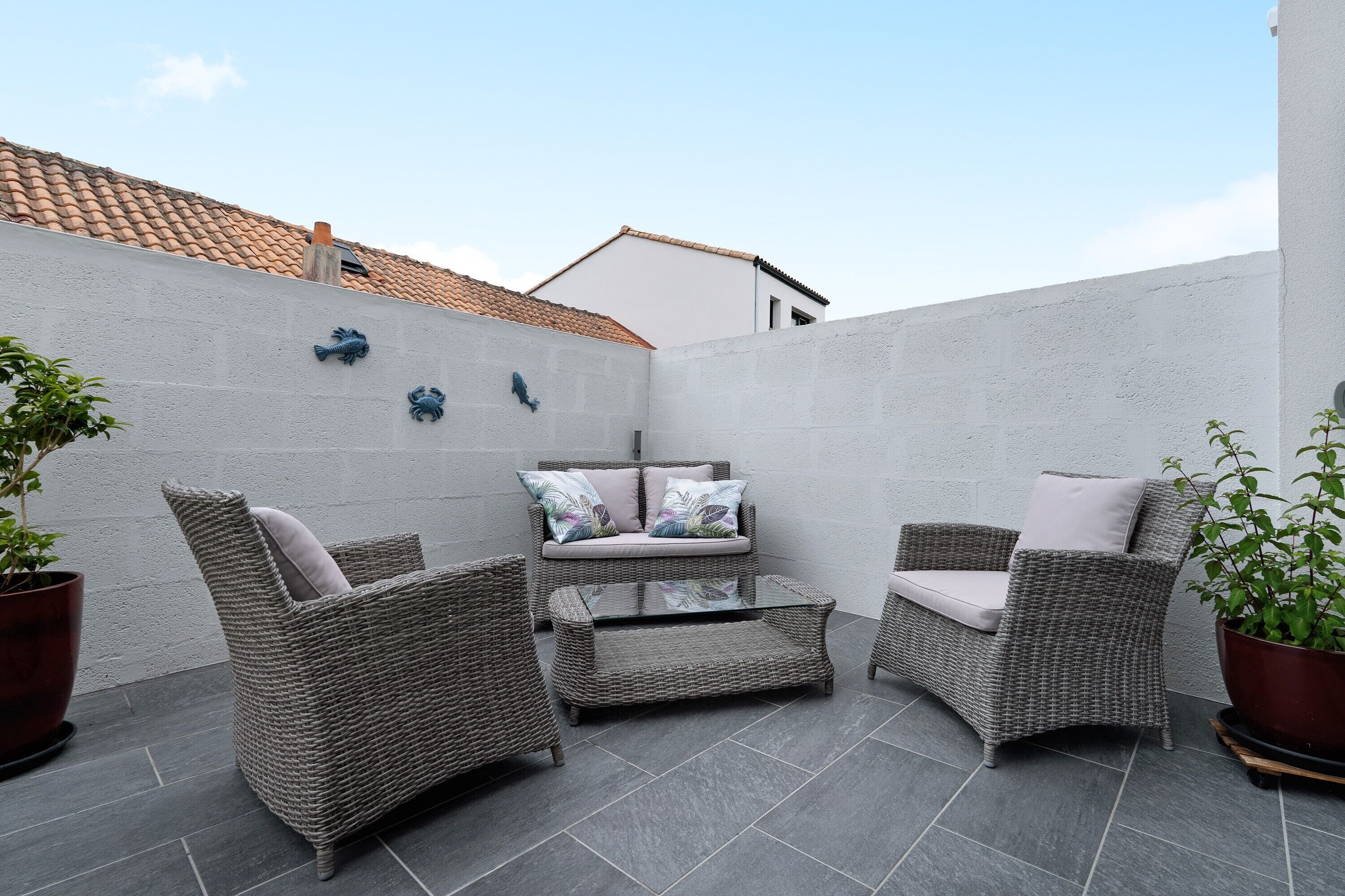 A patio with wicker furniture, a glass coffee table, and potted plants.