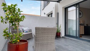 Eine Terrasse mit Korbmöbeln, einem Topfpflanzen und einer Schiebetür zu einem Innenraum.
