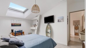 Ein Schlafzimmer mit Dachfenster, einem Bett mit blauer Bettwäsche, einem Fernseher und Kunstwerken an den Wänden.