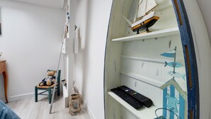 Ein Zimmer mit einem Holzbett, einem kleinen Tisch, einem Regal mit einem Modellschiff und einer Wandablage mit Tastatur und Dekoration.