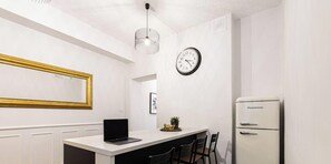 Uma cozinha moderna com bancada branca, um laptop, um relógio e uma geladeira.