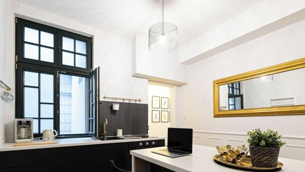 A modern kitchen with a large window, a laptop on the counter, and a mirror with a gold frame. - Verde 5 Gda sk Pok j z Azienk Blisko Centrum (Gdańsk)