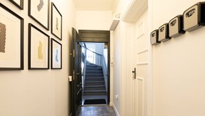 A hallway with framed artwork on the walls, a staircase leading to another floor, and a door with a keypad lock. - Verde 5 Gda sk Pok j z Azienk Blisko Centrum (Gdańsk)