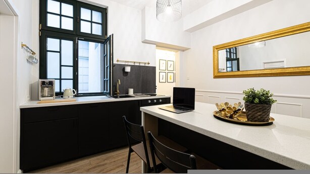 Une cuisine moderne avec une grande fenêtre, un ordinateur portable posé sur le plan de travail et un miroir au-dessus de l’évier.