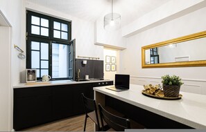 Een moderne keuken met een groot raam, een laptop op het aanrecht en een spiegel boven de wastafel.