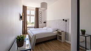 Habitación de hotel moderna con cama, mesitas de noche, lámpara, ventana con cortinas y vistas a zonas verdes.