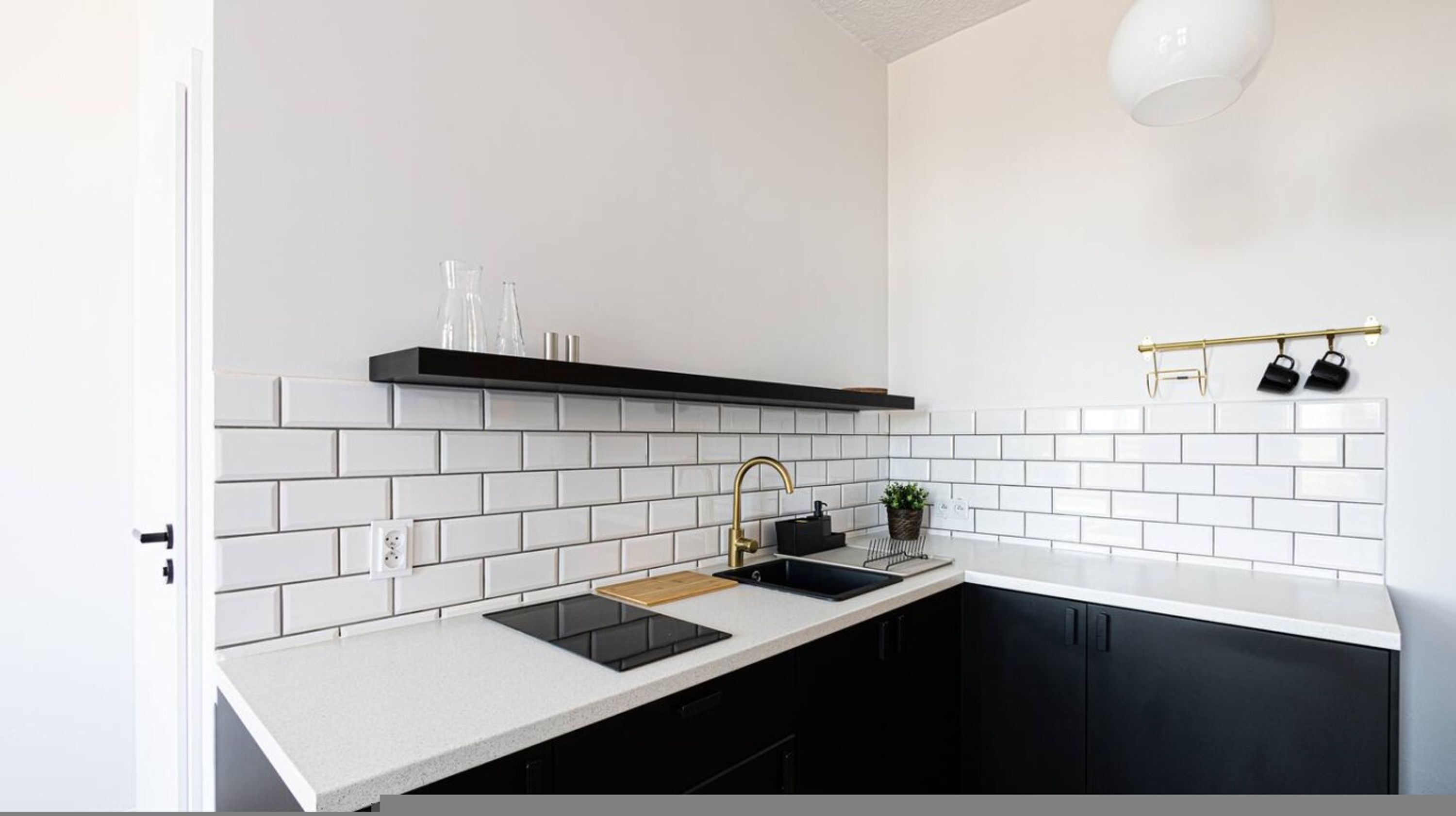 Una cocina moderna con azulejos blancos tipo metro, gabinetes negros, encimera negra, grifo dorado y estante con cristalería.