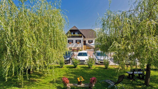 A house with a sloped roof, parked cars, and a grassy lawn with a bench and a small table with flowers. - Haus Anna in Rastovača - Plitvicer Seen / Haus Anna in Rastovača - Einzelzimmer ED1 (Plitvicka Jezera)