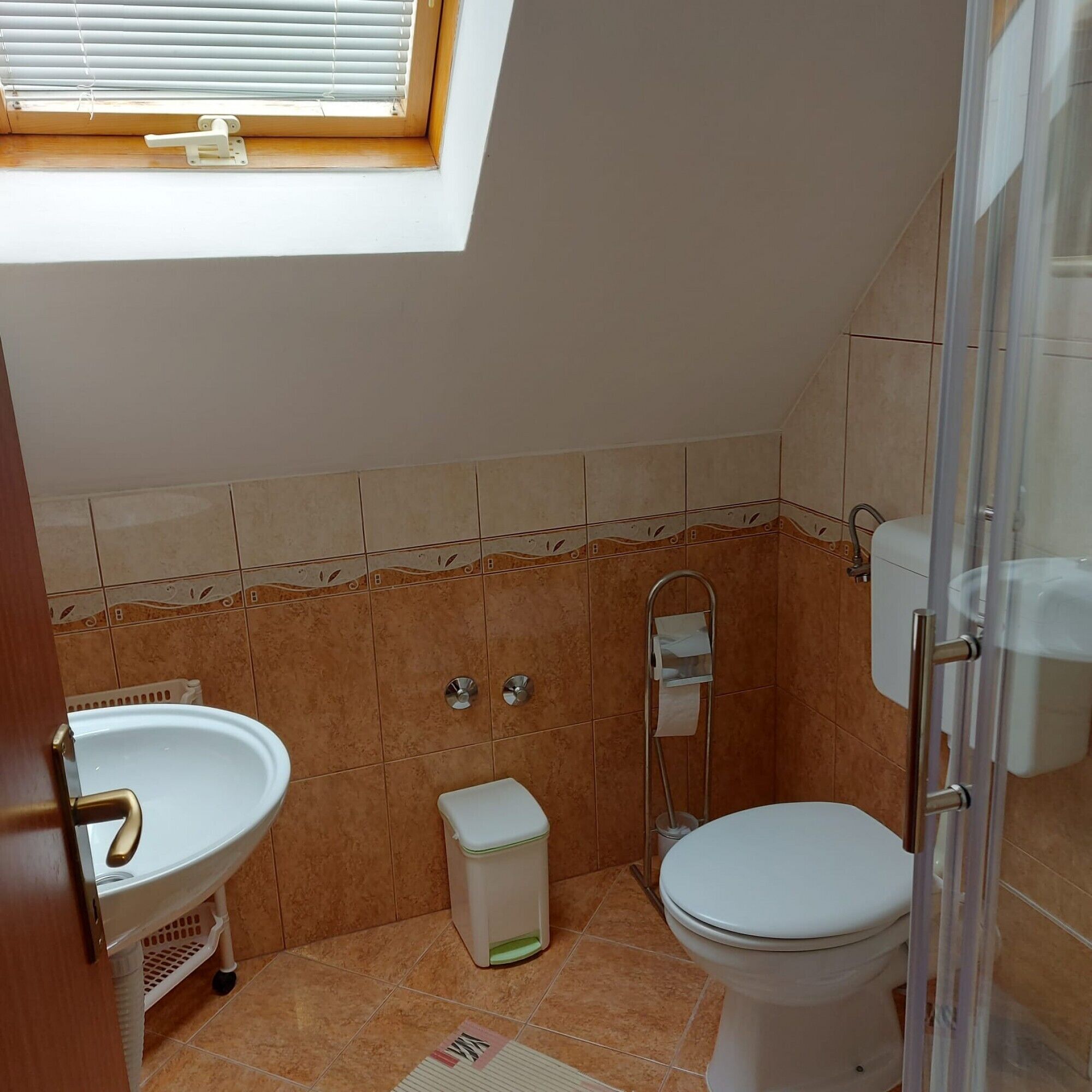 A compact bathroom with a skylight, a toilet, a sink, and a shower.