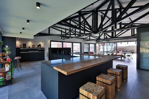 Une cuisine moderne dotée d’un îlot central, de tabourets de bar et d’un plafond haut avec des poutres apparentes.