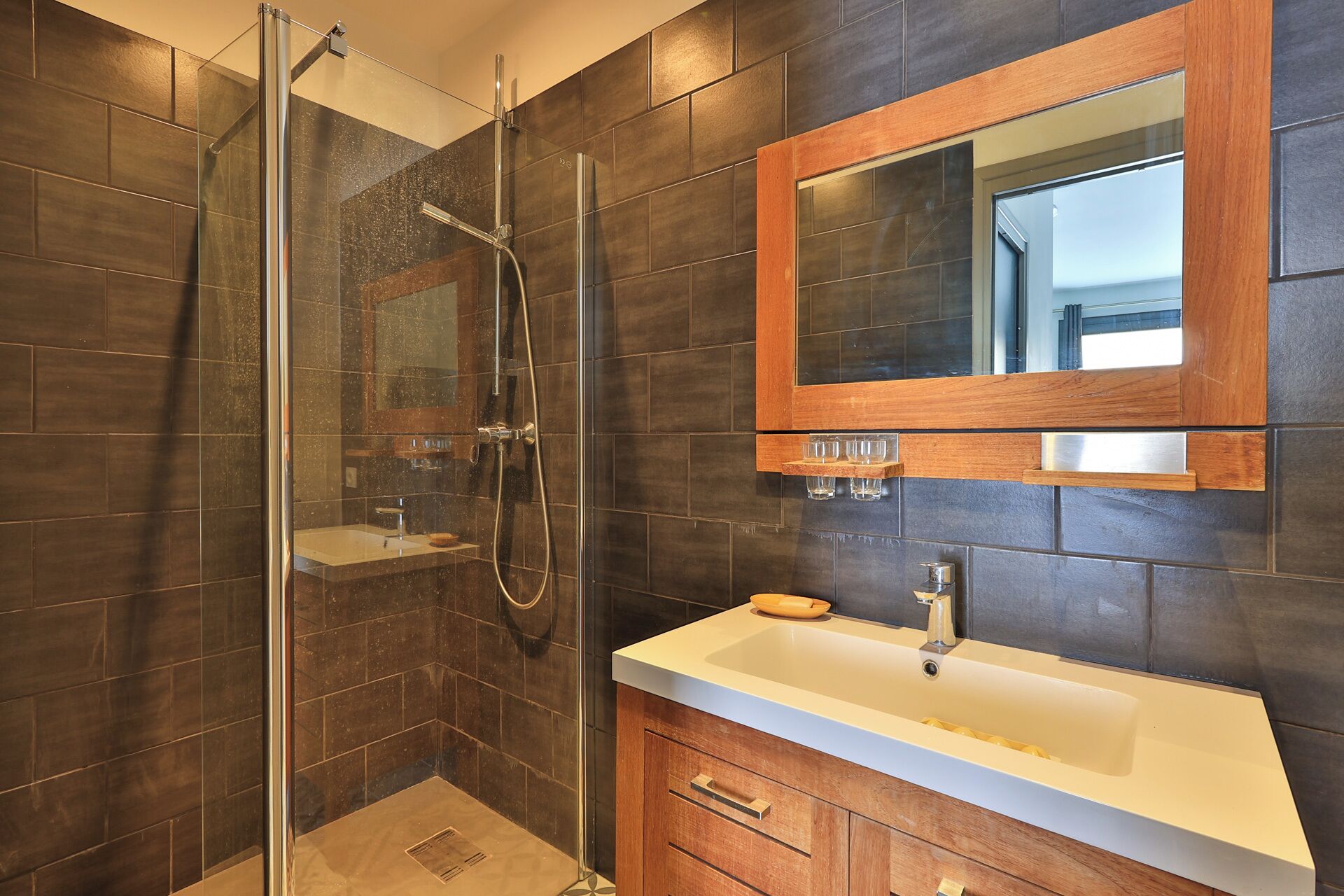 Une salle de bain dotée d’une douche à parois de verre, d’un meuble-lavabo en bois et d’un miroir placé au-dessus du meuble-lavabo.