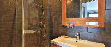 Une salle de bain dotée d’une douche à parois de verre, d’un meuble-lavabo en bois et d’un miroir placé au-dessus du meuble-lavabo.