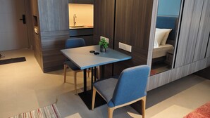 A modern, compact room with a dining table, chairs, a small plant, and a mirror reflecting a bed. - Cozy 1-bedroom studio in peaceful Langkawi with AC and gym access, kitchen (Langkawi)