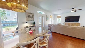 A spacious living room with a large sofa, a dining table with chairs, a TV, and a ceiling fan. - Flamingo Cove |New Listing|Private Beach Access|4BR Luxury Home|Pet Friendly (Miramar Beach)