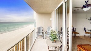 En balkon med udsigt over stranden, en ventilator i loftet og et bord med stole.
