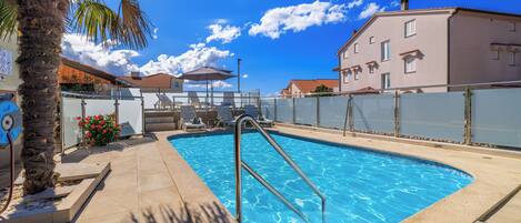 A swimming pool with a metal ladder, lounge chairs, and a palm tree.
