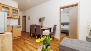 A modern kitchen with wooden cabinets, a dining area with a table and chairs, a grey sofa, and a bedroom visible through an open door. - Quiet apartment with pool, terrace and parking in Crikvenica (Crikvenica)