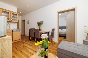A modern kitchen with wooden cabinets, a dining area with a table and chairs, a grey sofa, and a bedroom visible through an open door. - Quiet apartment with pool, terrace and parking in Crikvenica (Crikvenica)