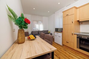 Une cuisine moderne avec des meubles en bois, une table à manger agrémentée d’un panier de fruits, et un coin salon avec un canapé et des rideaux.