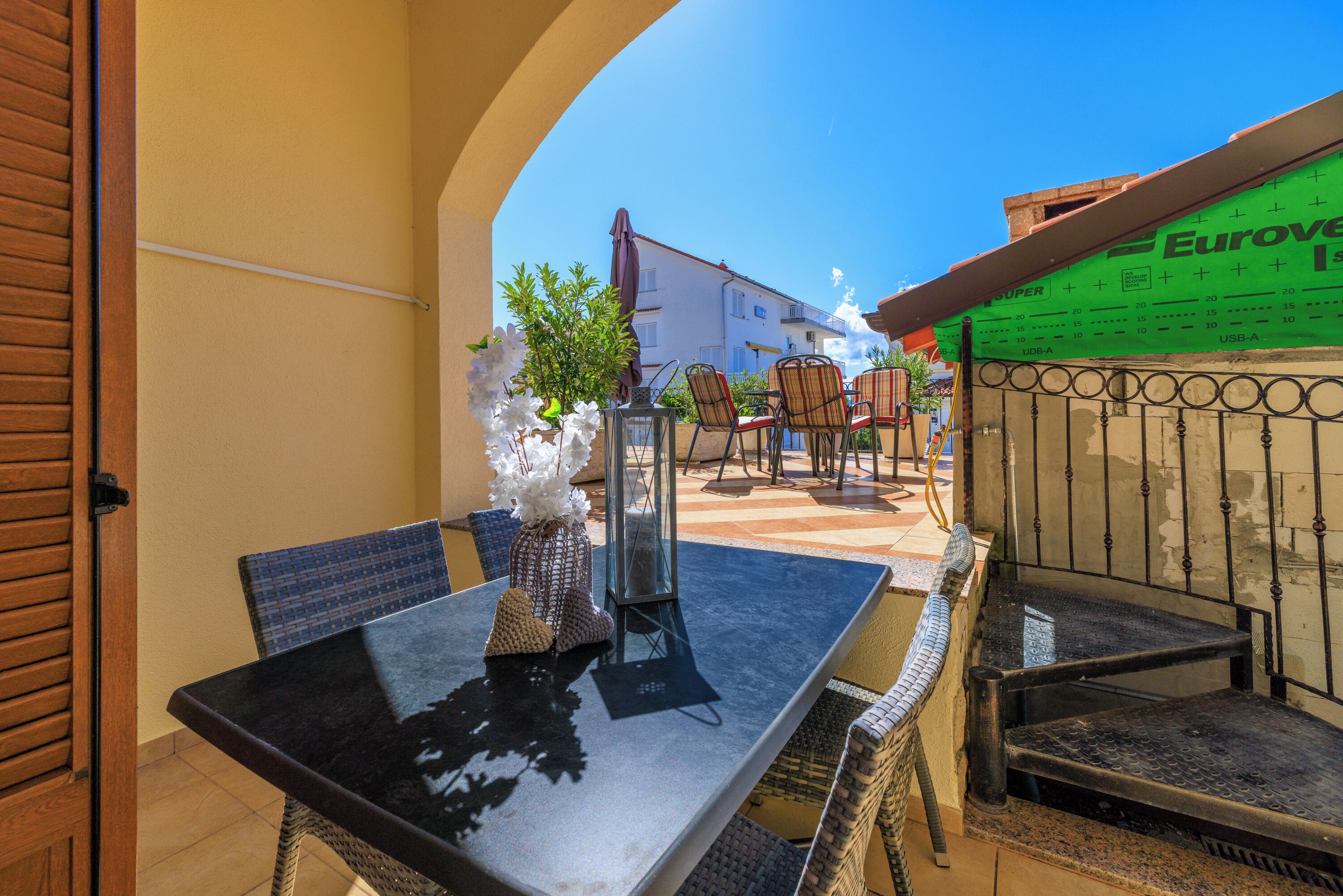 An outdoor patio with a table and chairs, a potted plant, and a metal gate.