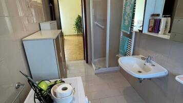 A bathroom with a shower, sink, toilet, and a small cabinet.