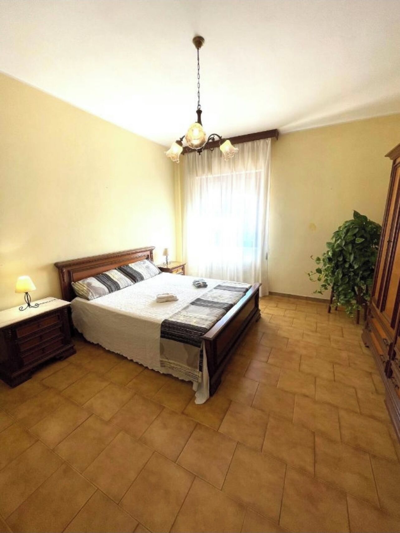 A bedroom with a bed, nightstand, lamp, and a hanging light fixture.