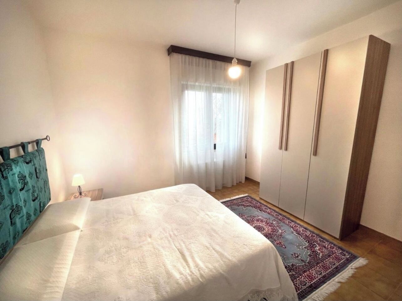 Ein Schlafzimmer mit Bett, Kleiderschrank, Nachttisch und einem Fenster mit Vorhängen.