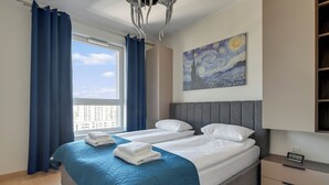 A hotel room with a bed, a nightstand, a painting, and a view of the city. - RentPlanet - Apartament Starowiejska (Gdańsk)