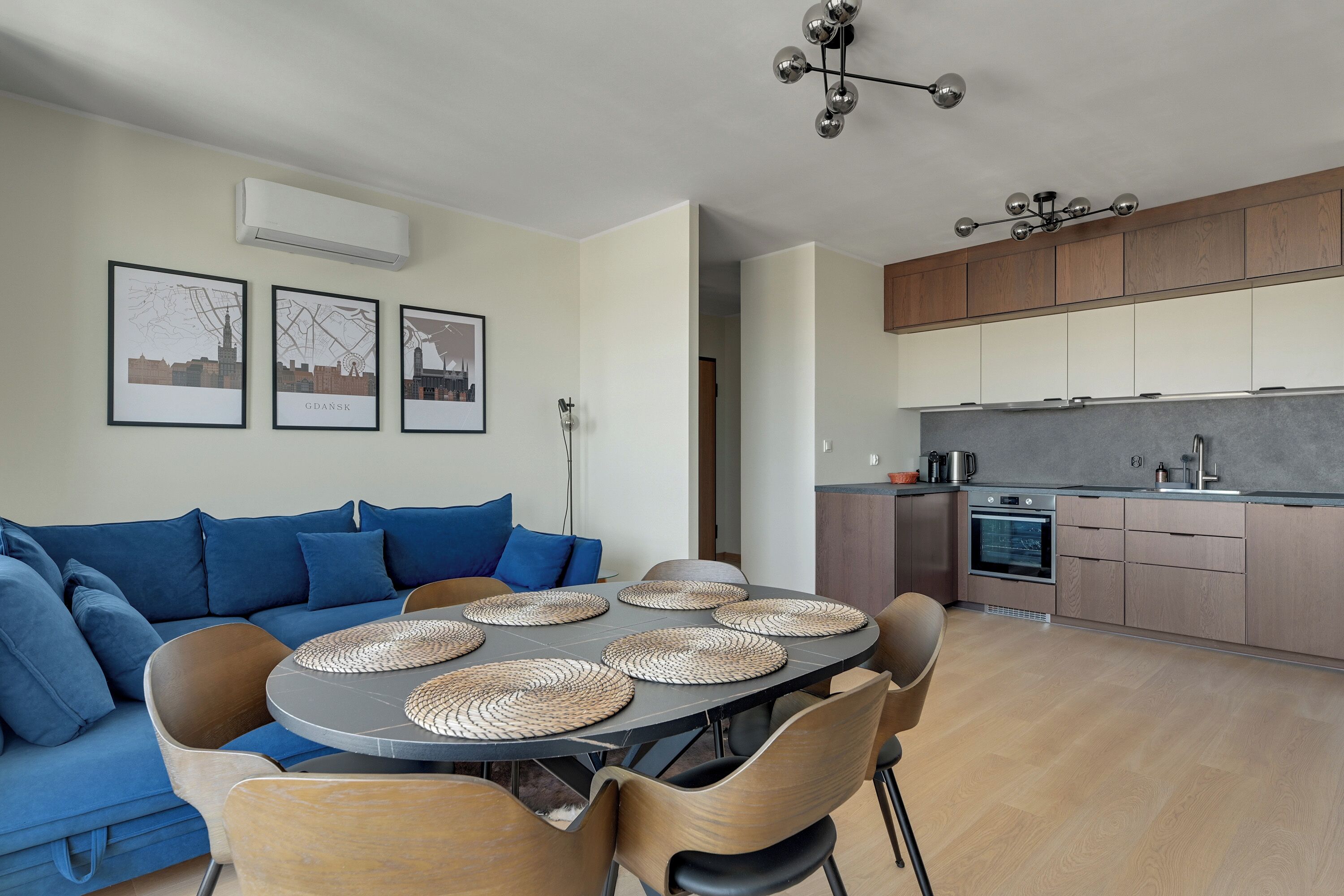 Un espacio habitable moderno con sofá, mesa de comedor, sillas, área de cocina y unidad de aire acondicionado instalada en la pared.