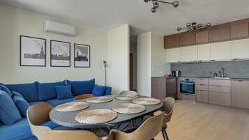 A modern living space with a sofa, dining table, chairs, kitchen area, and wall-mounted air conditioning unit.