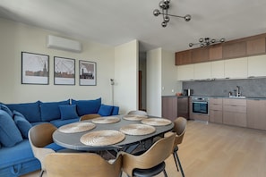 Um espaço de estar moderno com sofá, mesa de jantar, cadeiras, cozinha e ar condicionado fixado na parede.