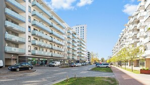A modern multi-story residential building with balconies, a paved street, and parked cars. - RentPlanet - Apartament Starowiejska (Gdańsk)