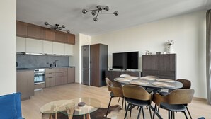 A modern kitchen with a dining area, a flat-screen TV, and a dining table with chairs. - RentPlanet - Apartament Starowiejska (Gdańsk)