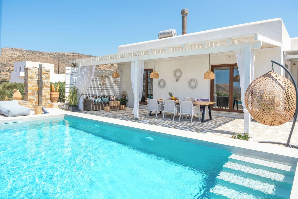 A poolside area with a clear blue pool, outdoor seating, and a pergola.