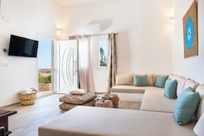 A modern living room with a sofa, a flat-screen TV, a wall-mounted air conditioner, and a large window with curtains.
