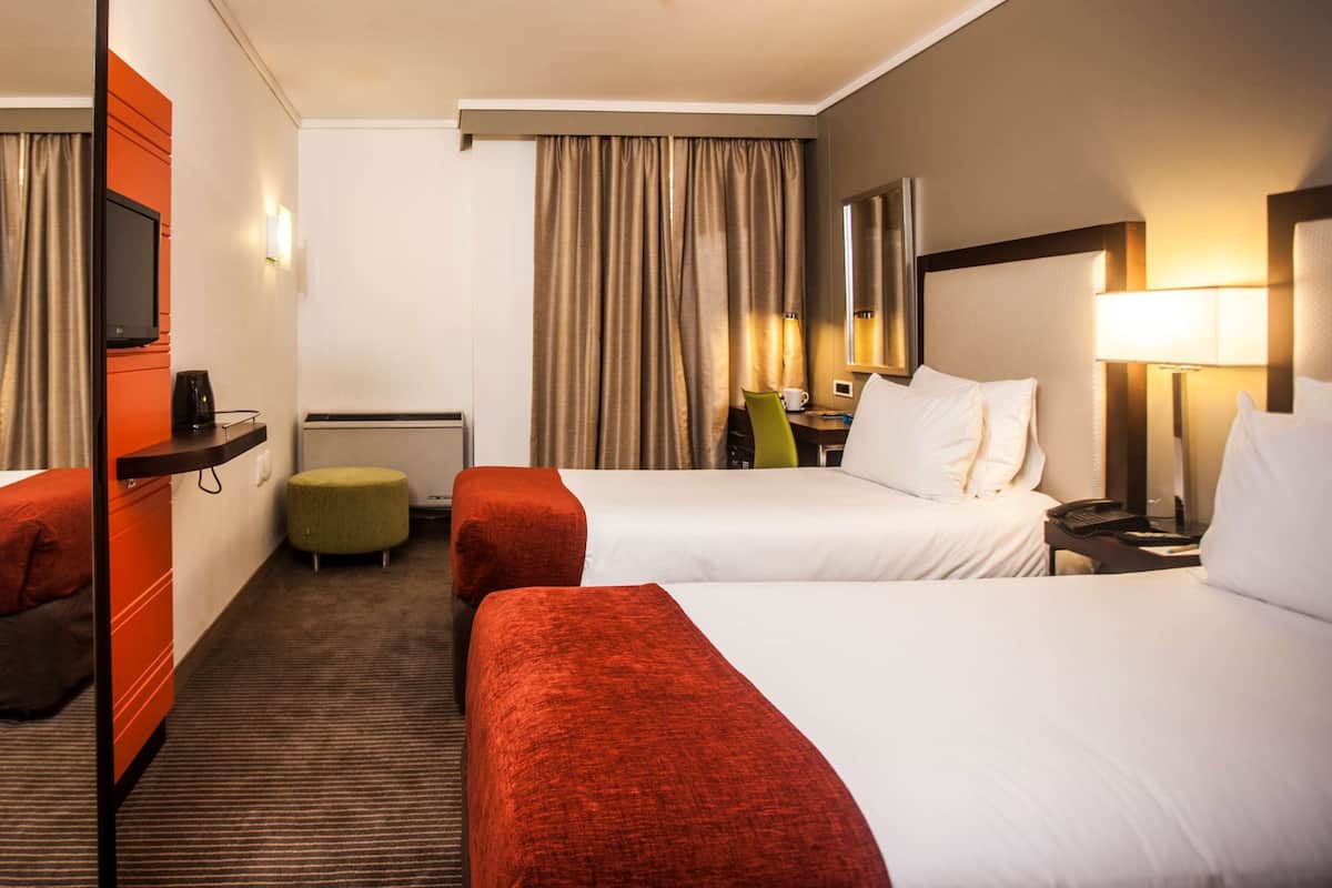 A hotel room with two beds, a desk, a chair, a television, and a window with curtains.