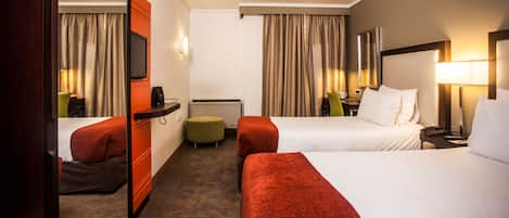 A hotel room with two beds, a desk, a chair, a television, and a window with curtains.