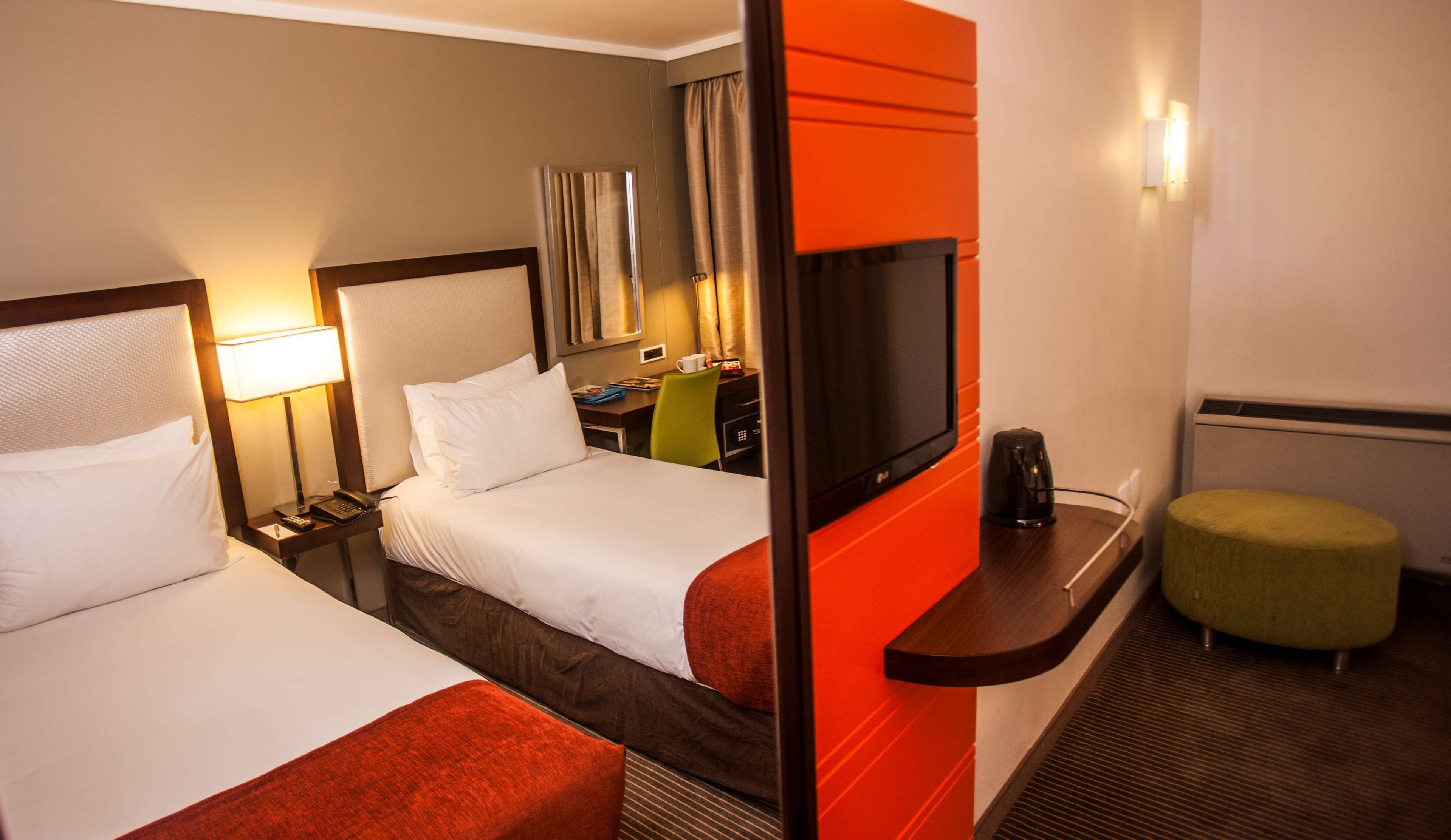 Habitación de hotel con dos camas, un escritorio, televisor, cafetera y un pequeño reposapiés.