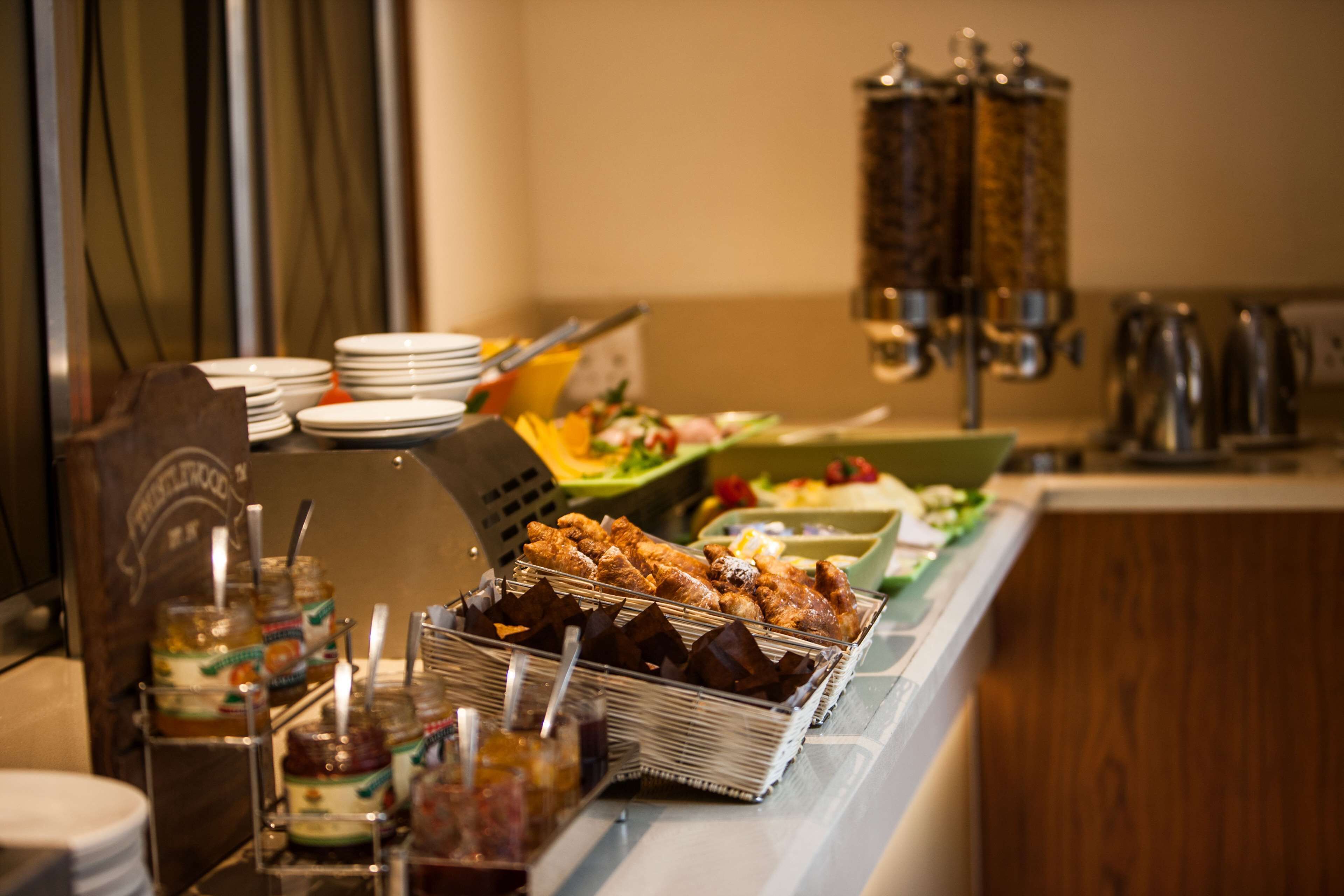 Uma mesa de buffet com diversos alimentos, recipientes de acompanhamentos e utensílios de servir.