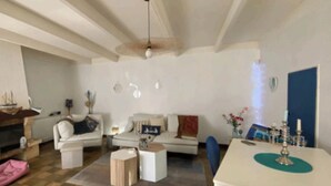 A living room with a sofa, coffee table, and a dining area with a table and chairs. - RESPIRER A DEUX EN FINISTERE NORD (Taulé)