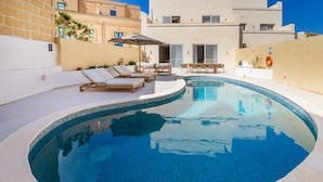 A swimming pool with lounge chairs, a table, and a covered seating area. - Casa Elana Holiday Gozitan Home (Xaghra)