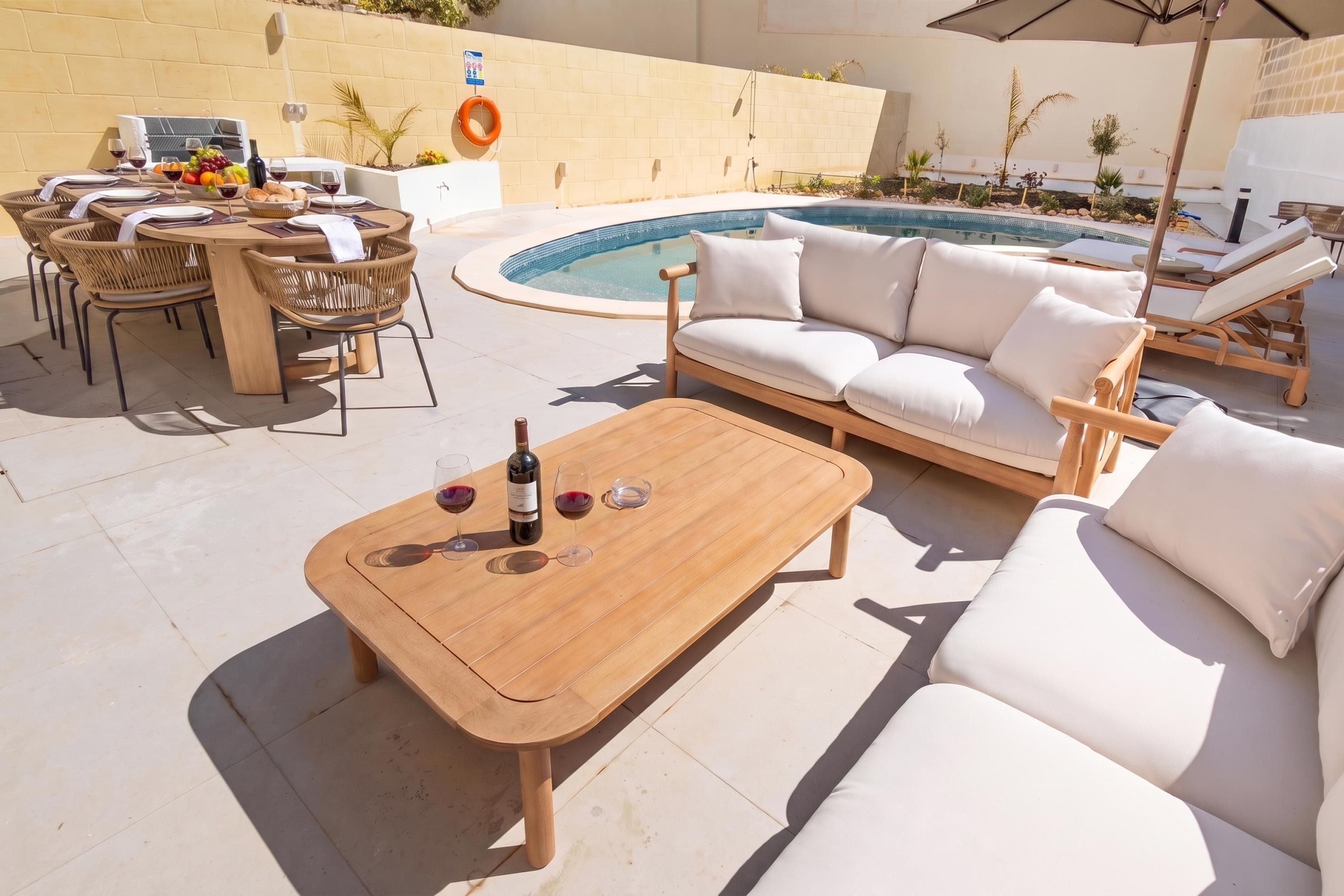 An outdoor seating area with a pool, a table with wine glasses, and a sofa.